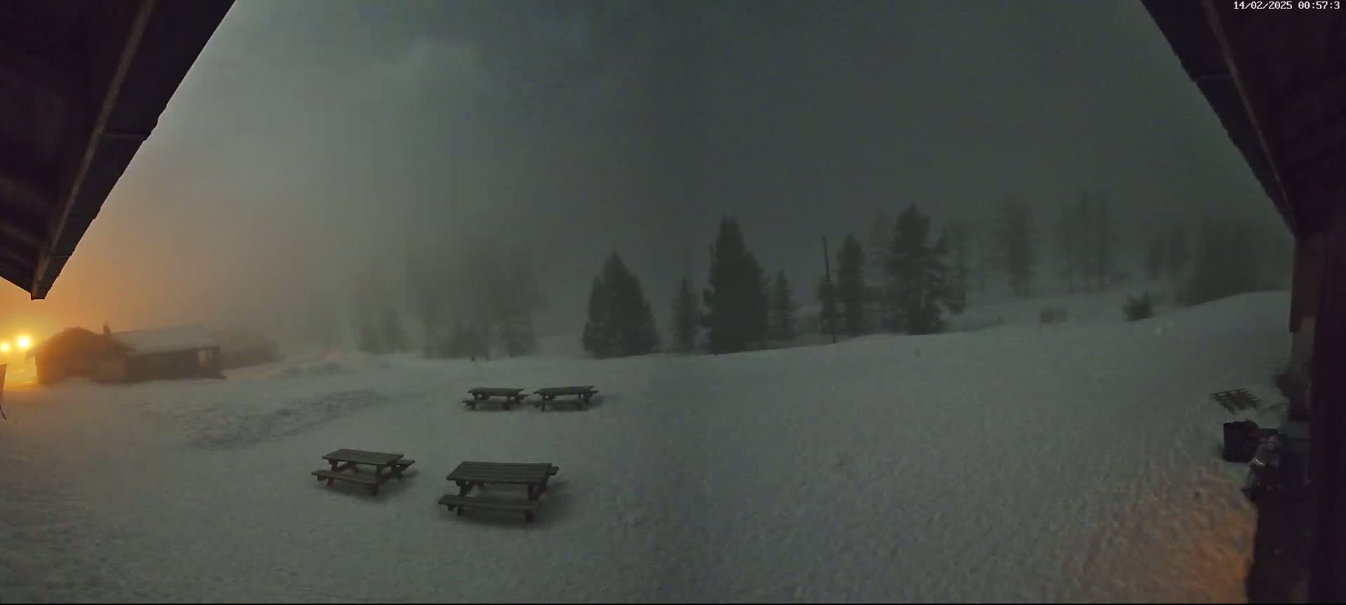 A snow-covered landscape is visible through a partially obscured view, showing several picnic tables and a building in the heavy fog or snow.