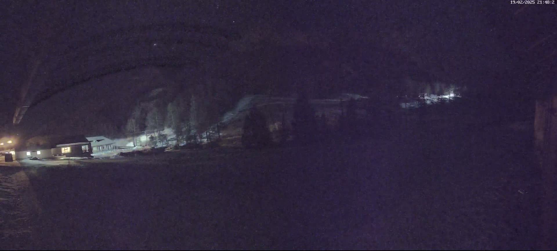 A nighttime, snowy scene shows a building illuminated by lights, surrounded by trees and a snow-covered landscape.