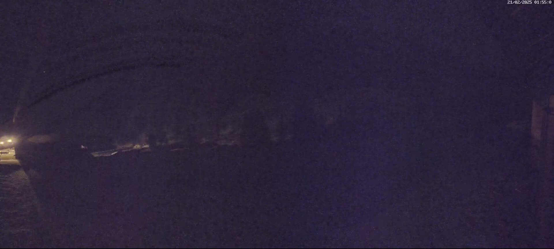 A dark, nighttime scene shows a blurry, snow-covered area under a curved structure, dimly lit by distant lights.