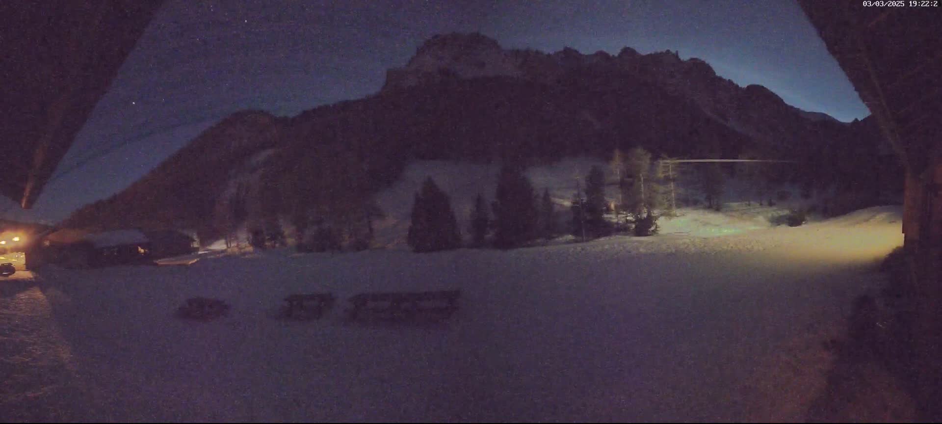 A nighttime view of a snow-covered landscape with a mountain in the background under a dark, starry sky.