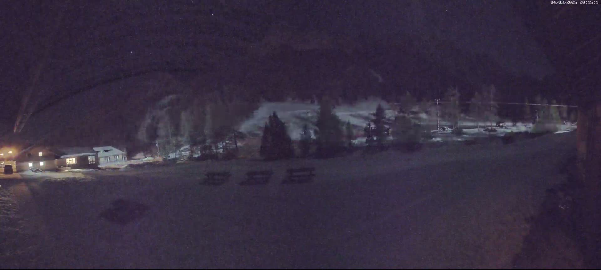A nighttime view of a snow-covered area with a building and trees, under a dark, possibly snowy sky.
