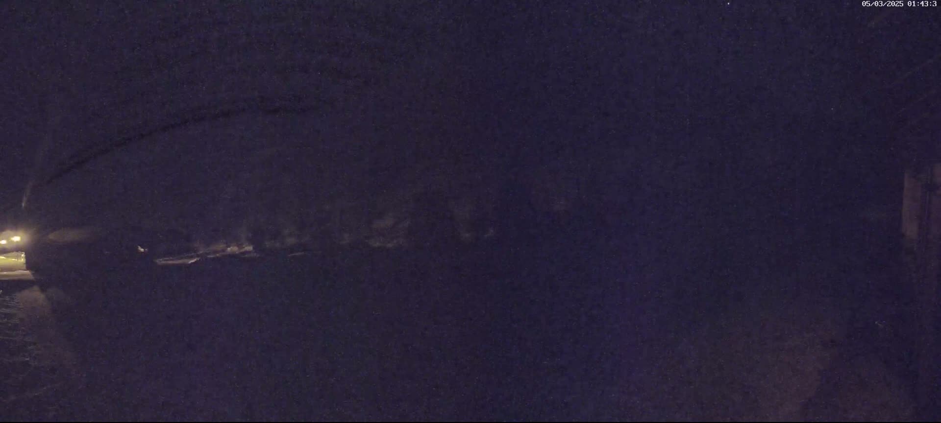 A dark, nighttime scene shows a snow-covered area with a vehicle partially visible under dimly lit conditions.