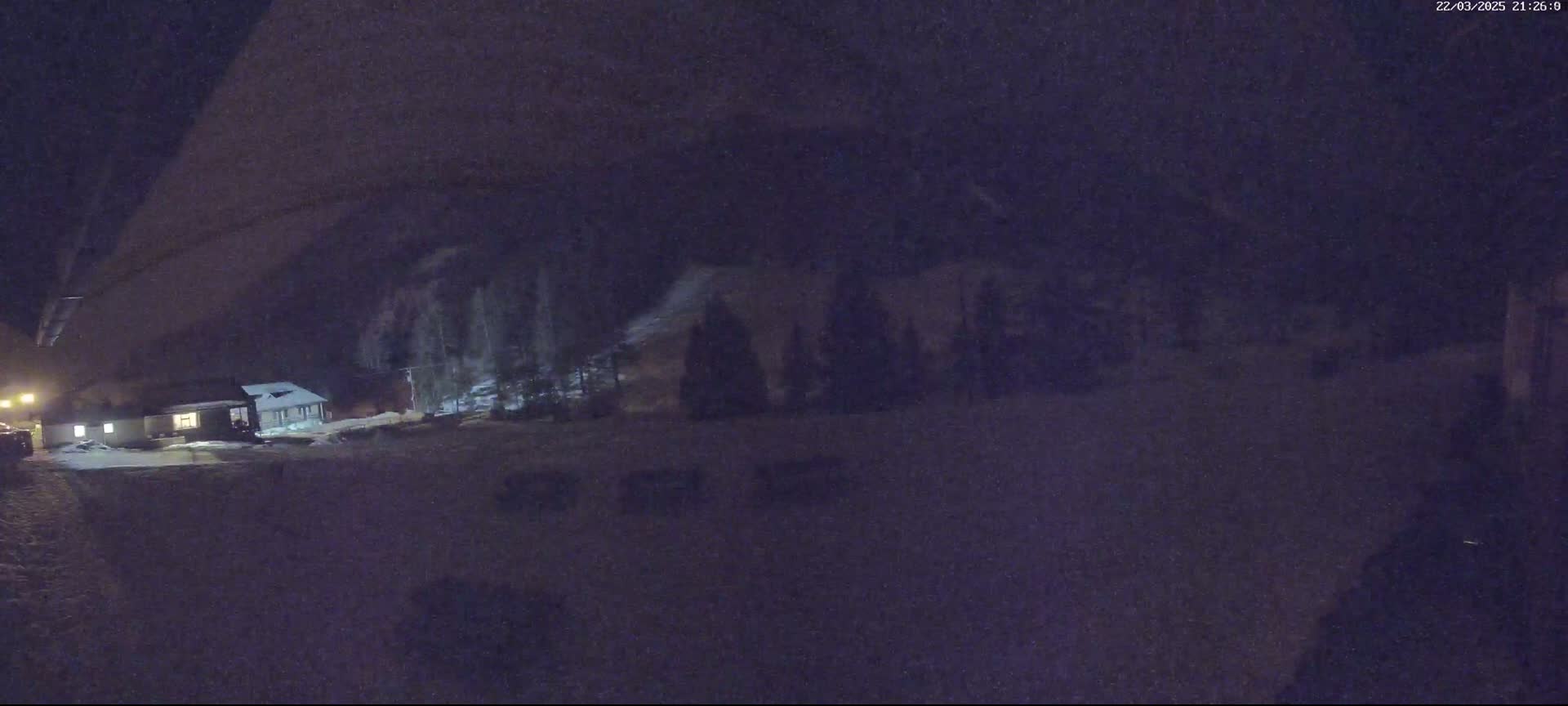 A dimly lit nighttime scene shows a snow-covered building and a few trees under a dark, possibly snowy sky.