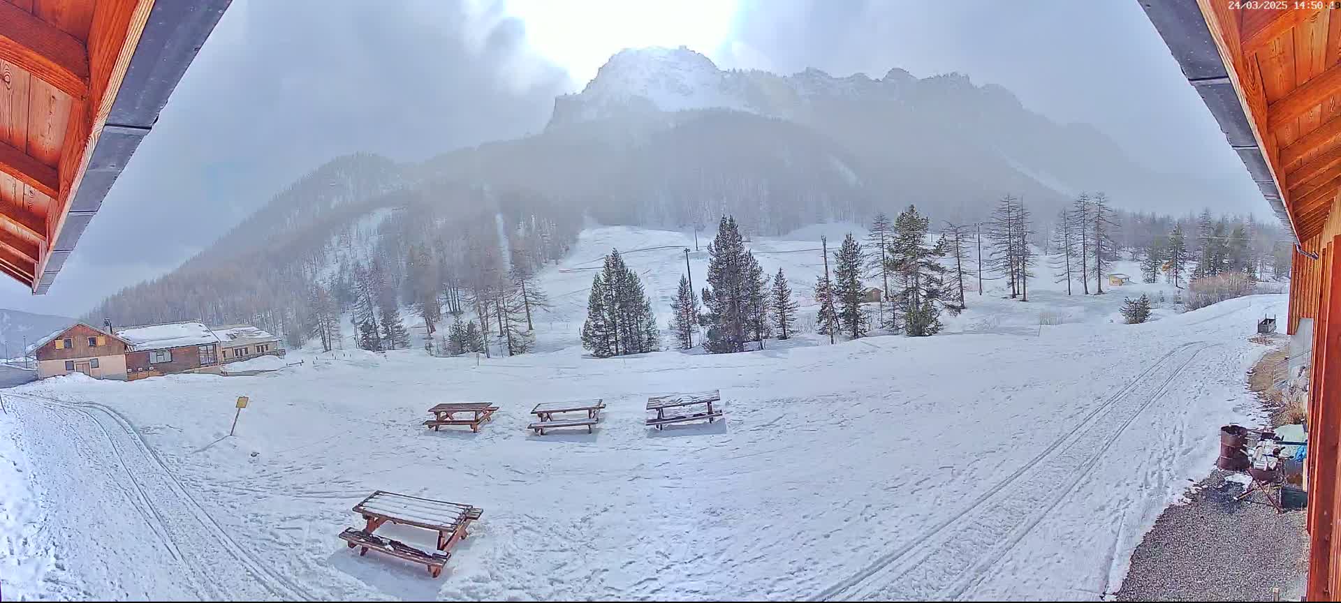 A snow-covered landscape with several picnic tables, a building, and a mountain in the background under hazy, bright conditions.