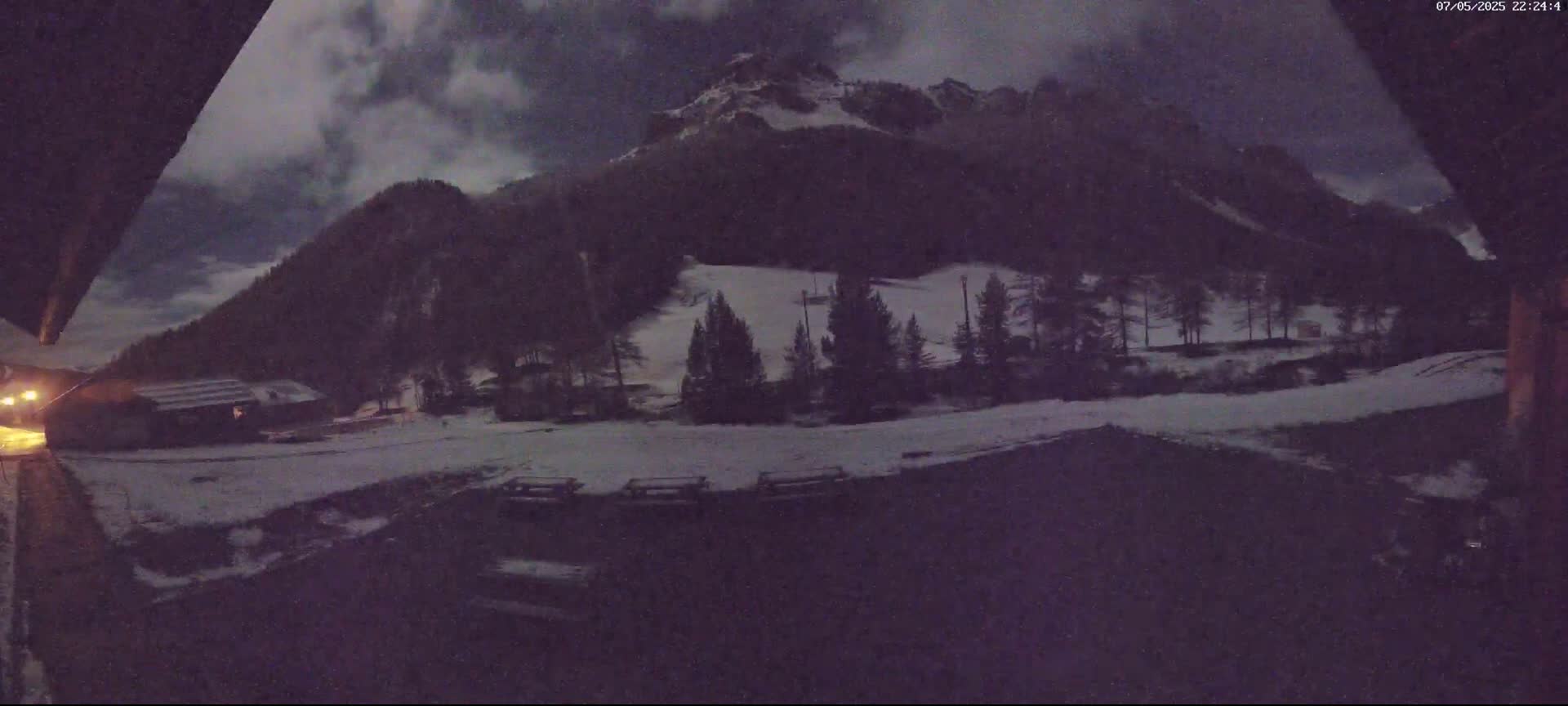 A nighttime view of snow-covered ground and a mountain range under a cloudy sky.