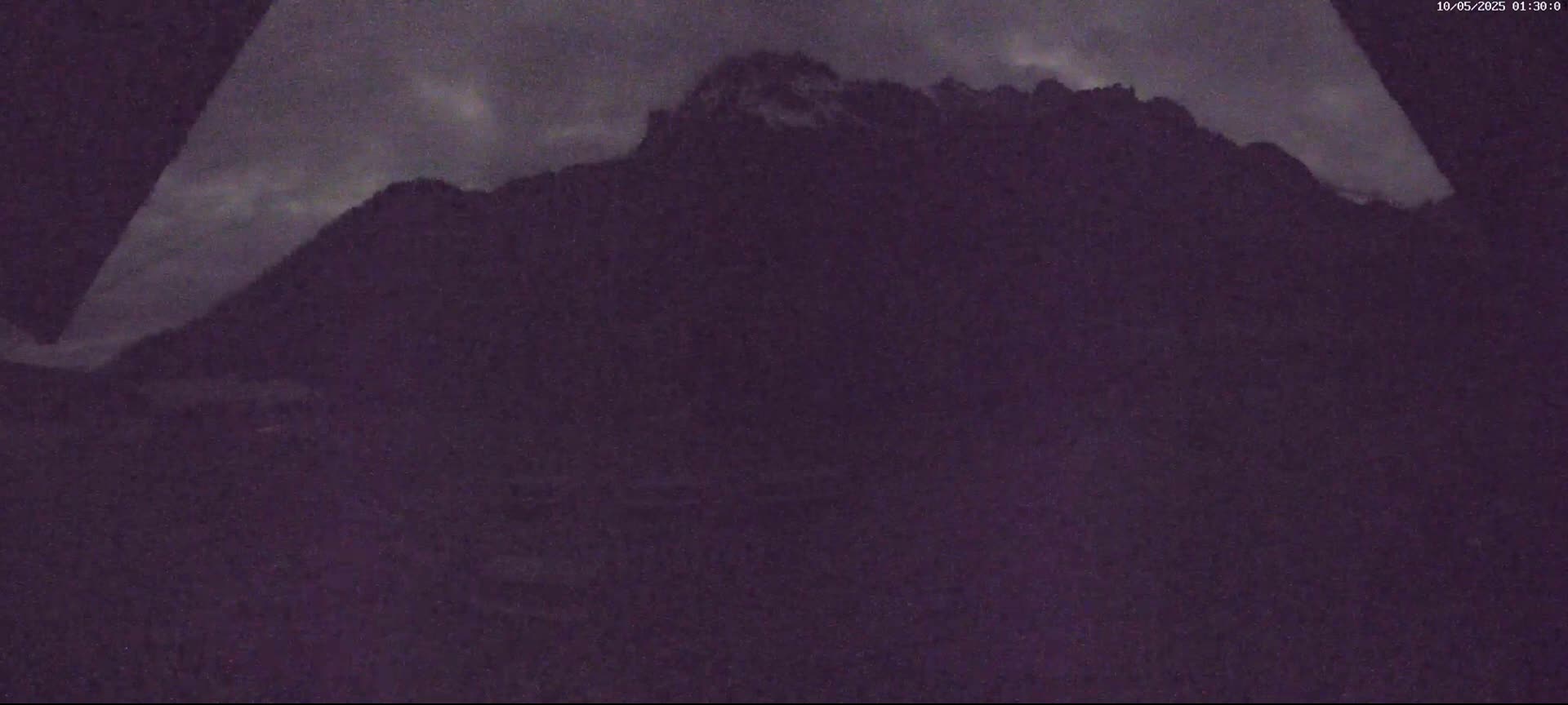 A dark, nighttime view shows a mountain range under a cloudy sky.