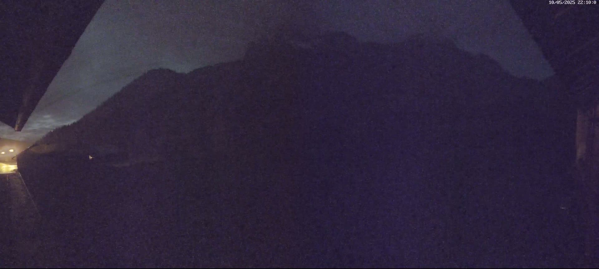 A dark, nighttime view shows a large, silhouetted mountain range under a cloudy sky.