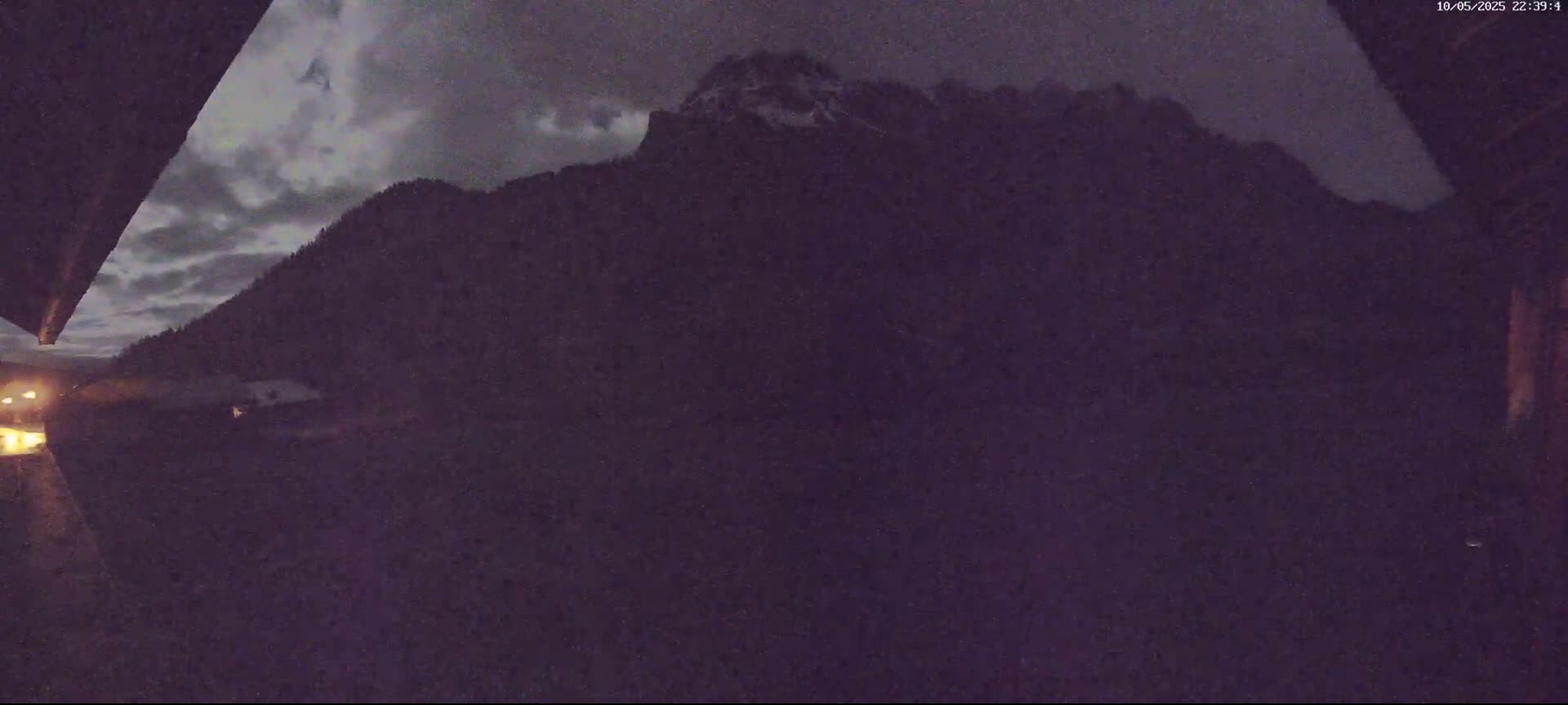 A nighttime view shows a snow-capped mountain range under a partly cloudy sky.