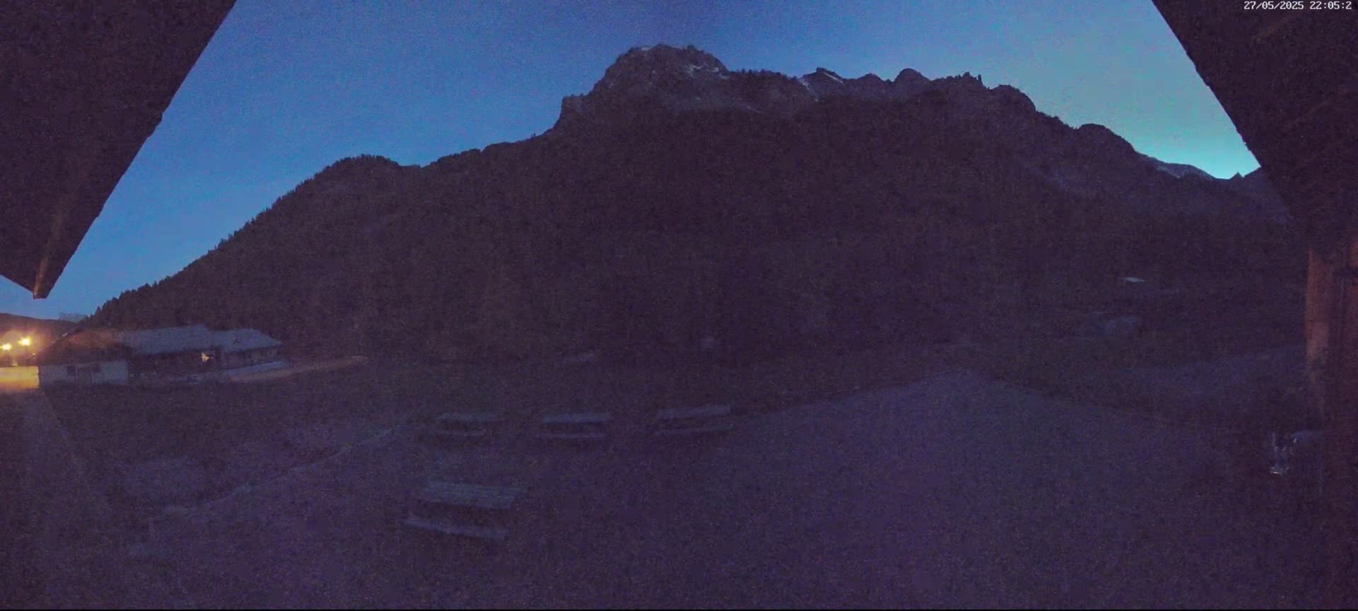 A dark, mountainous landscape is visible at twilight, with a building and some picnic tables in the foreground.