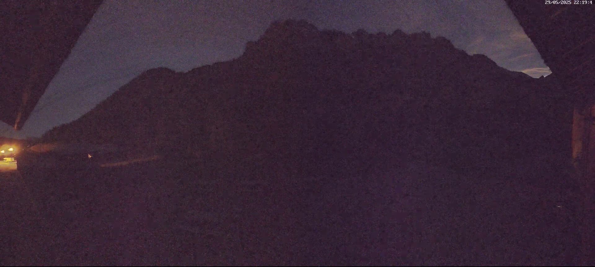 A dark, nighttime view shows a large, silhouetted mountain range under a twilight sky.