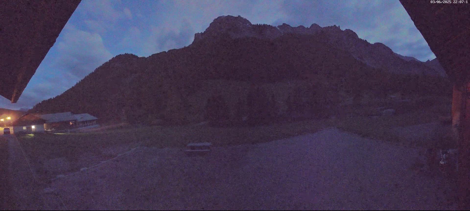 A dark, mountainous landscape is visible at dusk, with a building and a small, flat area in the foreground.