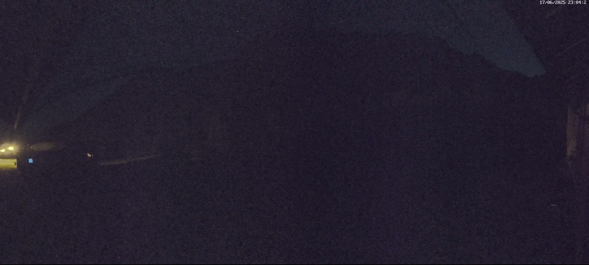 A dark, nighttime scene shows a vehicle parked near a building under a clear, dark sky.