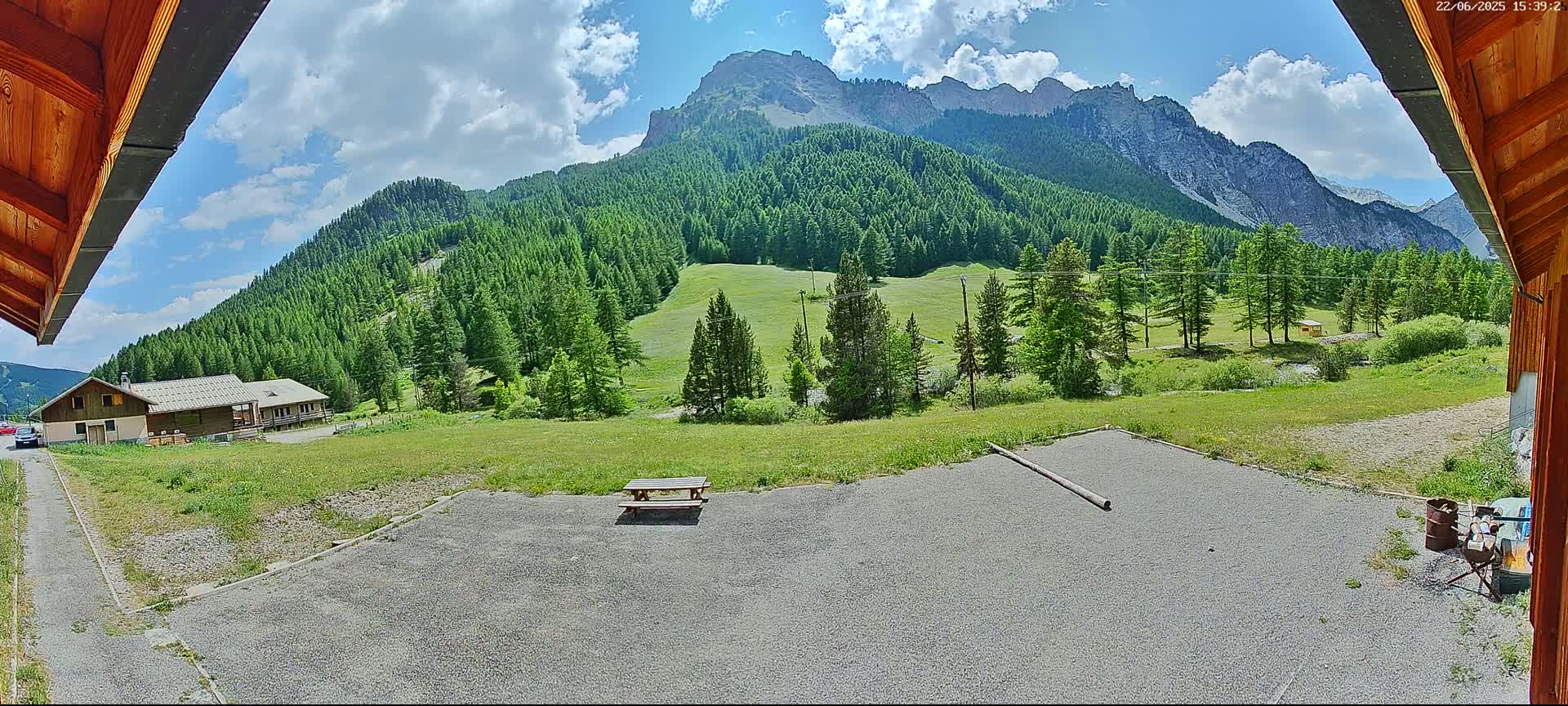 A gravel area with a picnic table overlooks a valley of green trees and mountains under a partly cloudy sky.