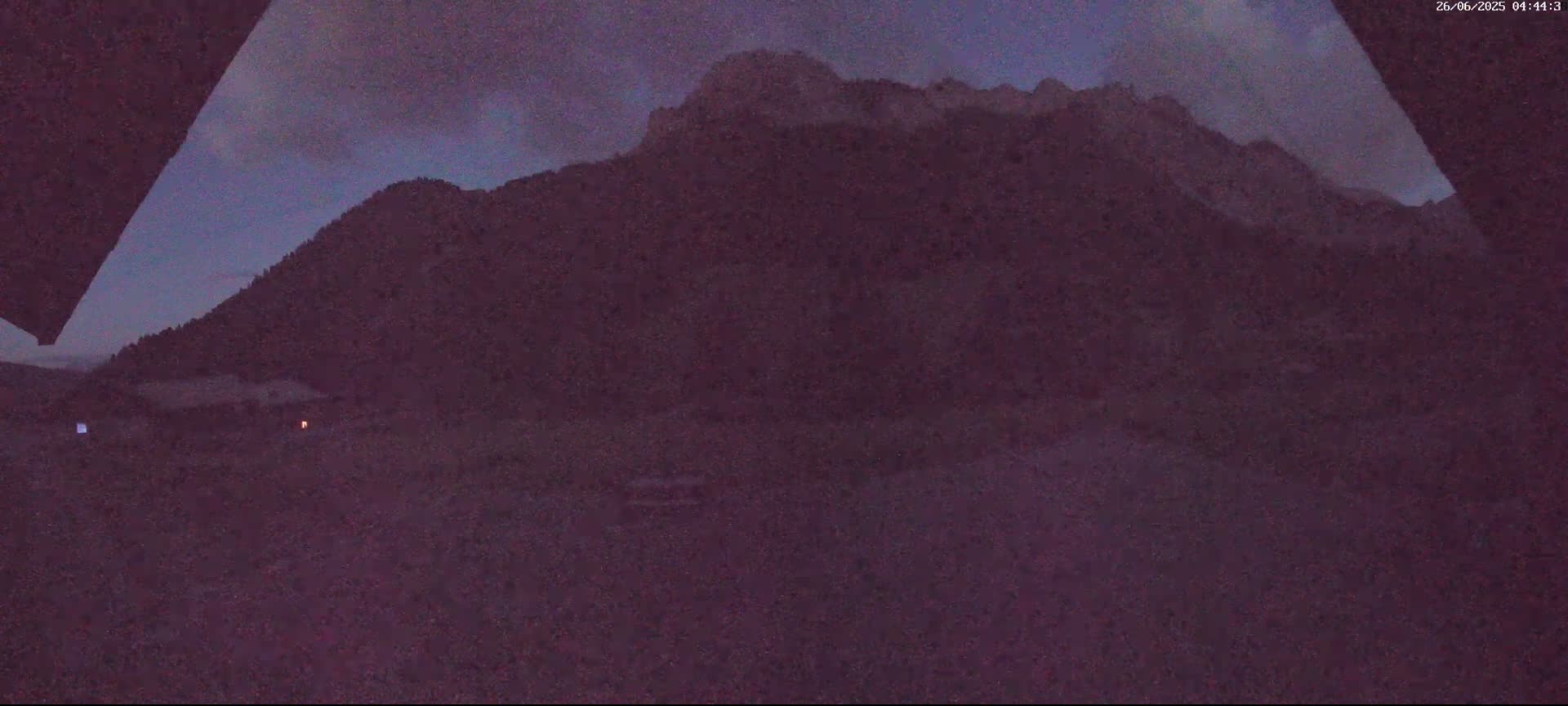A dark, mountainous landscape is visible at twilight, with a building and a faint light in the foreground.