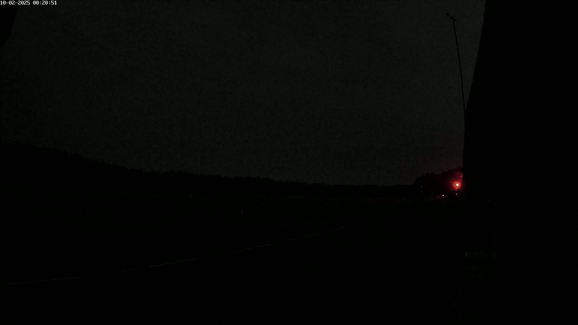 A dark, nighttime scene shows a dimly lit landscape with a single red light in the distance.
