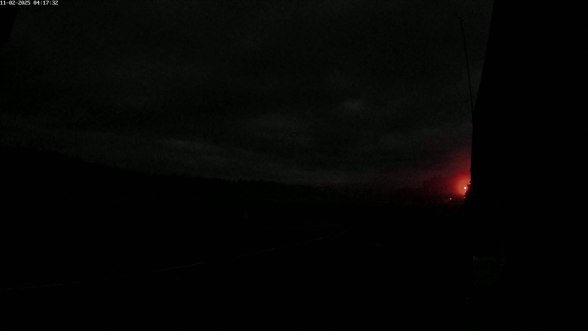 A dark, nighttime scene shows a faint red glow on the horizon under a mostly cloudy sky.