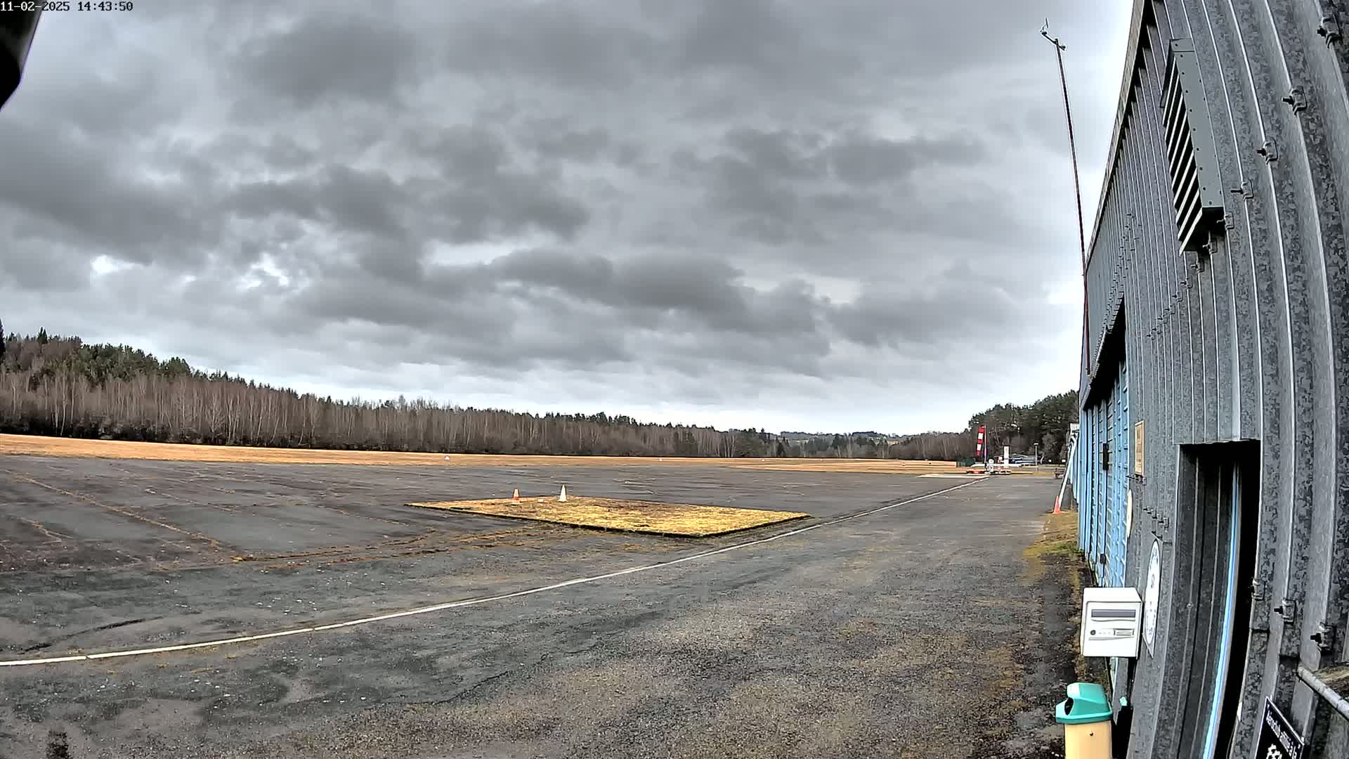 A small airfield with a mostly overcast sky stretches out before a corrugated metal building.