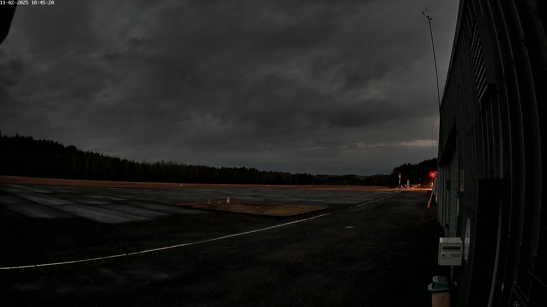 A dark, overcast sky looms over a deserted airfield next to a large, dark building.