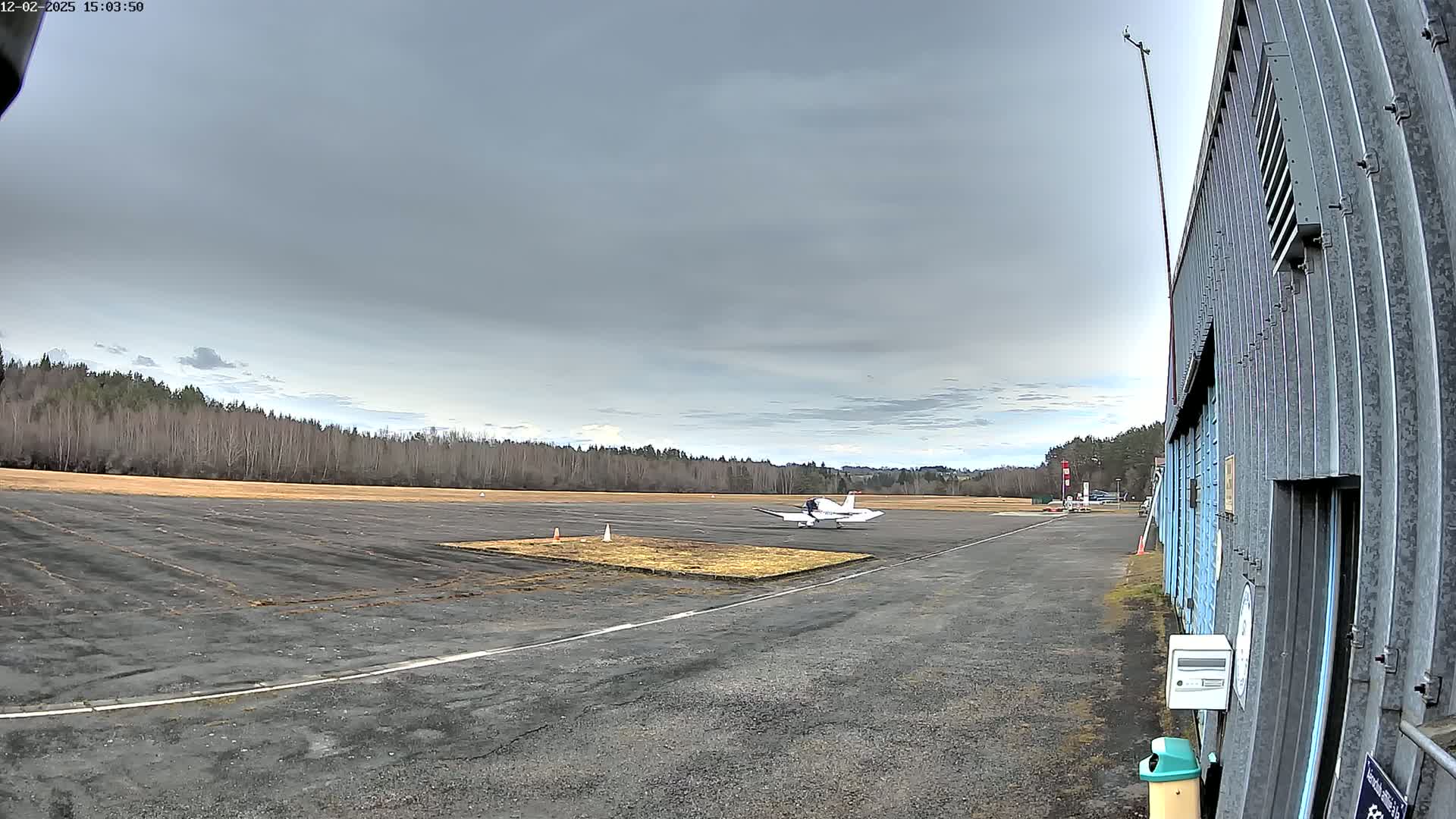 A small airplane sits on a tarmac next to a hangar under an overcast sky.