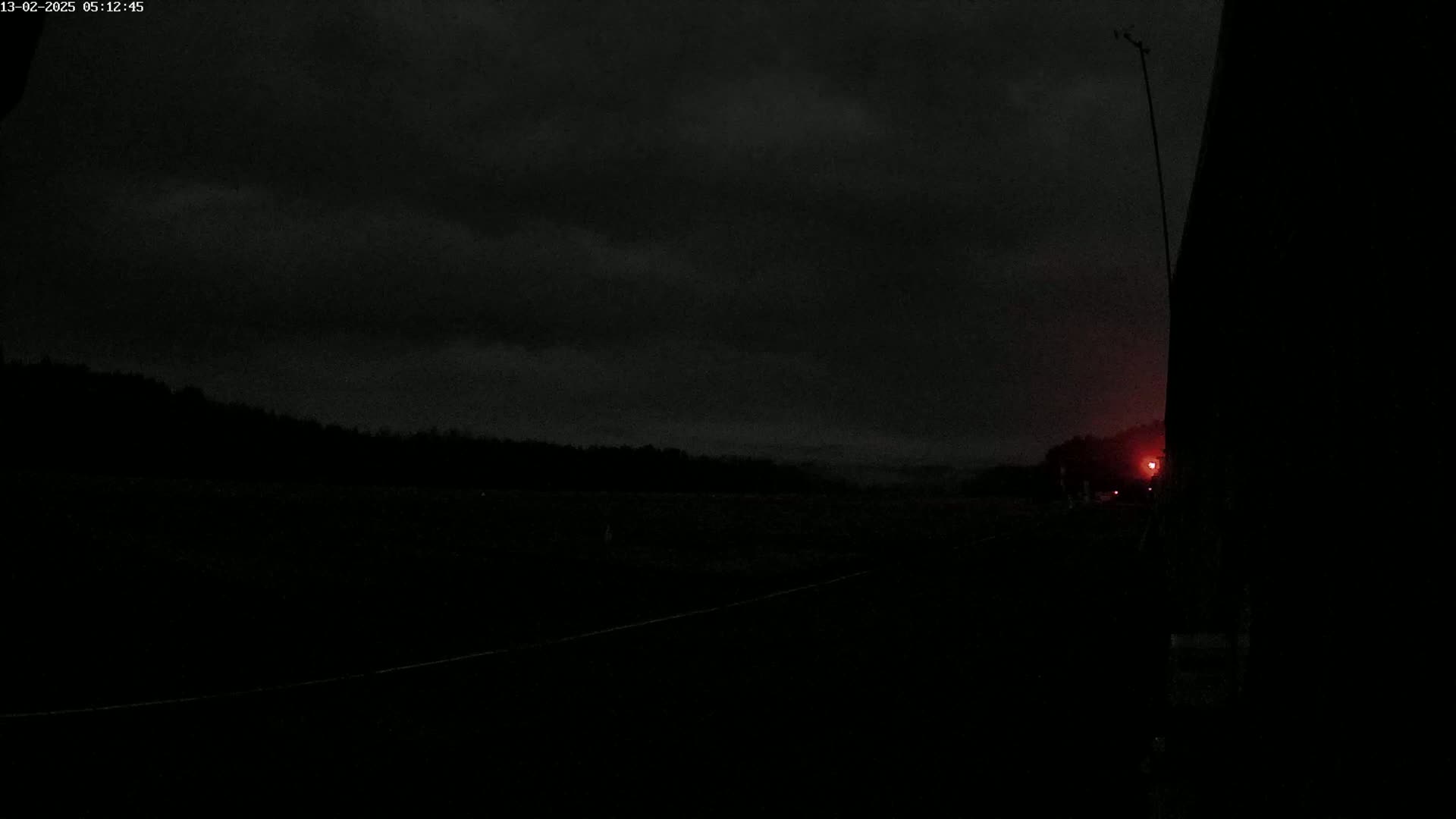 A dark, overcast night scene shows a road leading to a treeline under a dark sky.