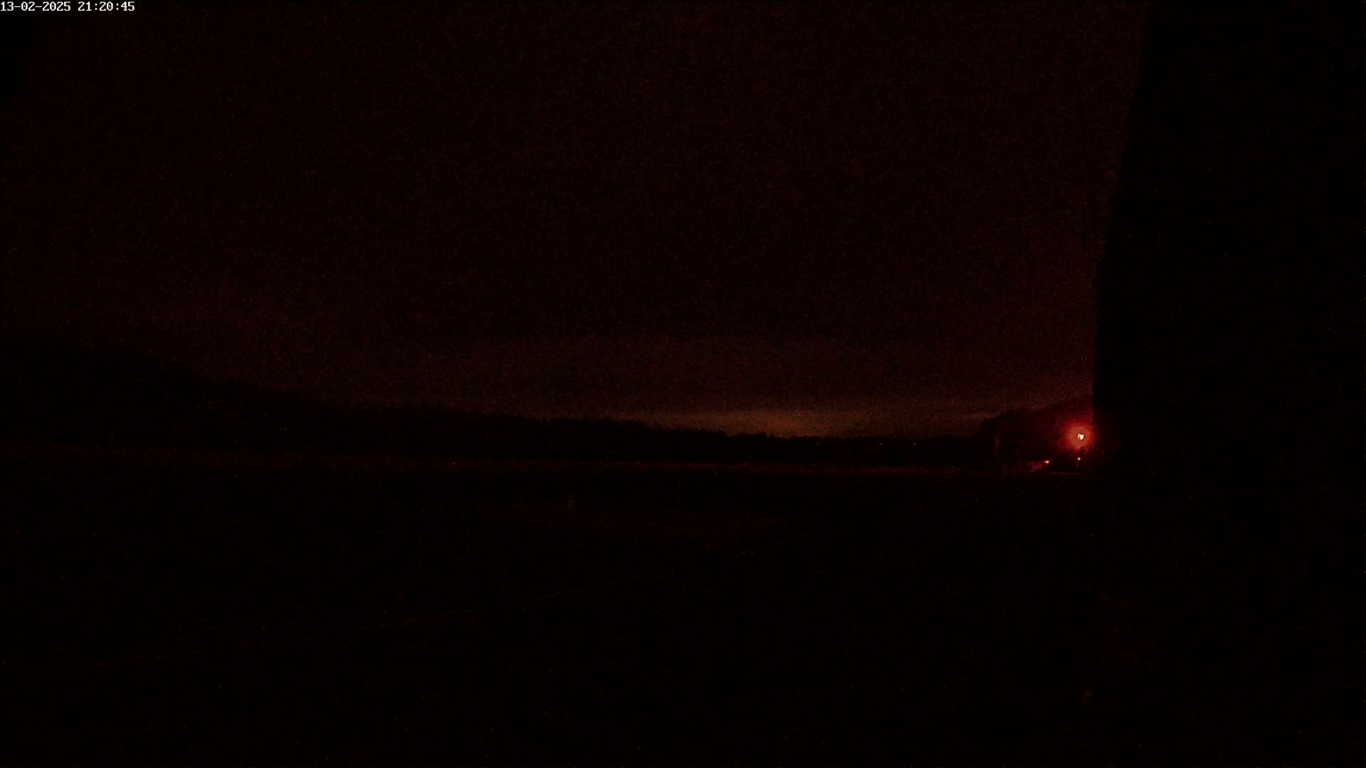 A dark, nighttime scene shows a flat landscape with a single distant red light and a dark, possibly silhouetted, object on the right.
