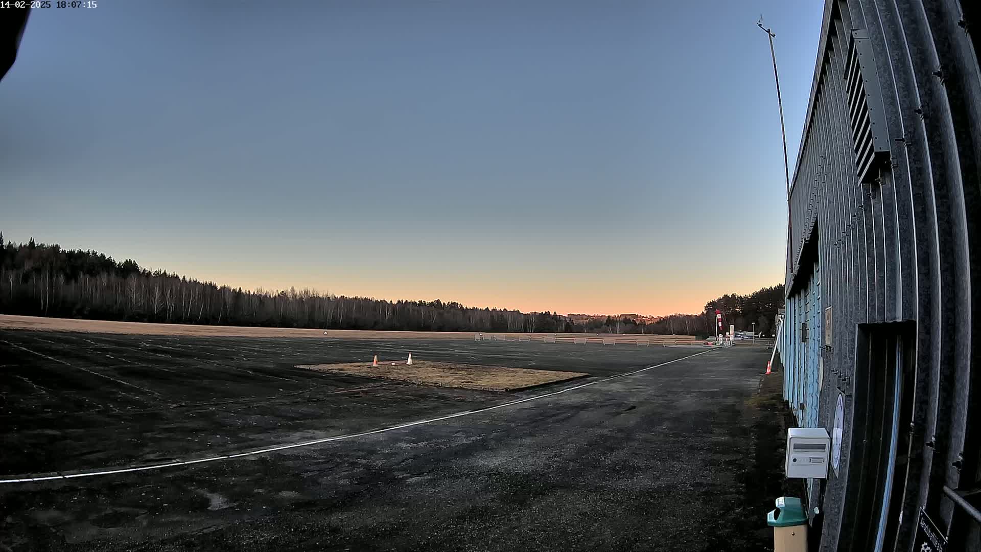A dark paved area, possibly a runway or parking lot, extends toward a line of trees under a twilight sky.