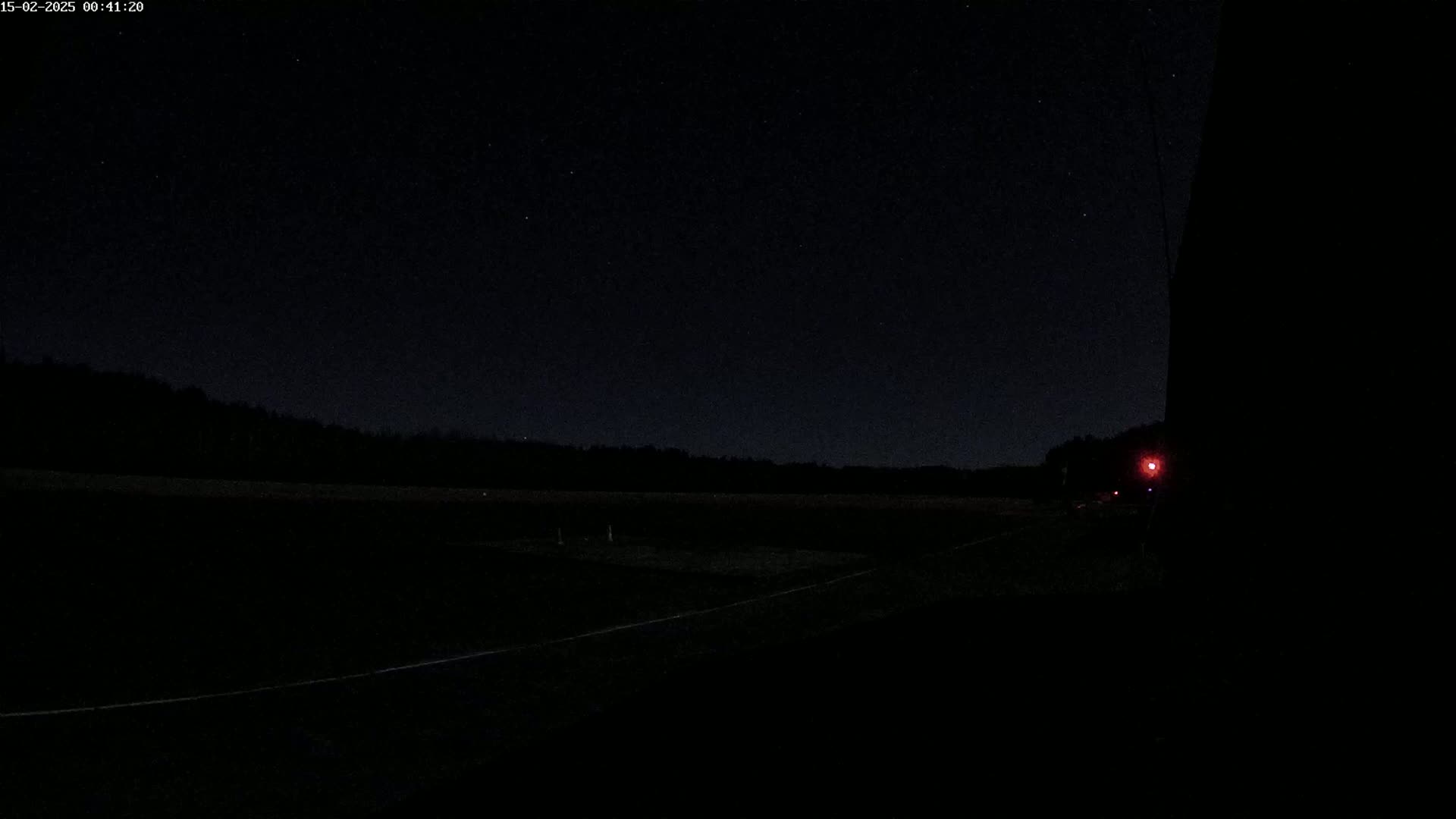 A dark, nighttime scene shows a flat, empty field with a faint line possibly marking a road or path under a clear, star-studded sky.