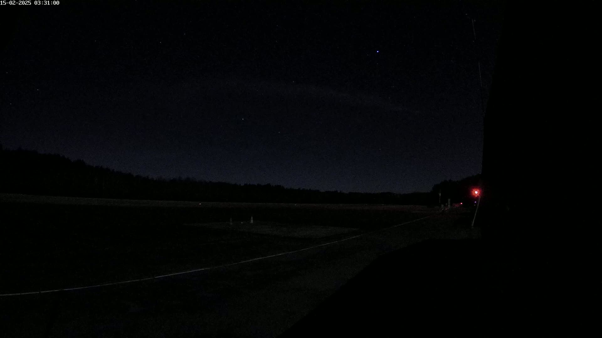 A dark, nighttime view of a road leading to a treeline under a clear, starry sky.