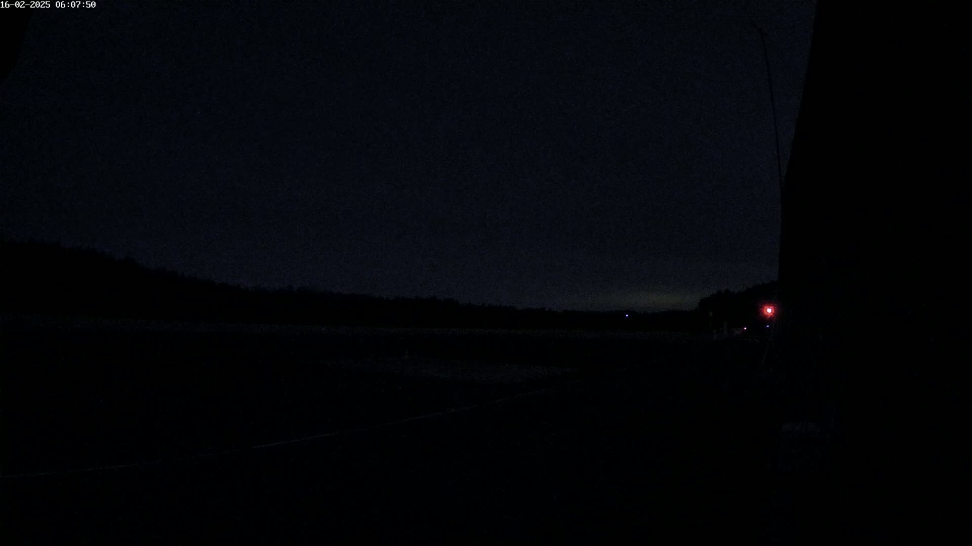 A dark, nighttime scene shows a flat, dark landscape with a faint red light visible in the distance.