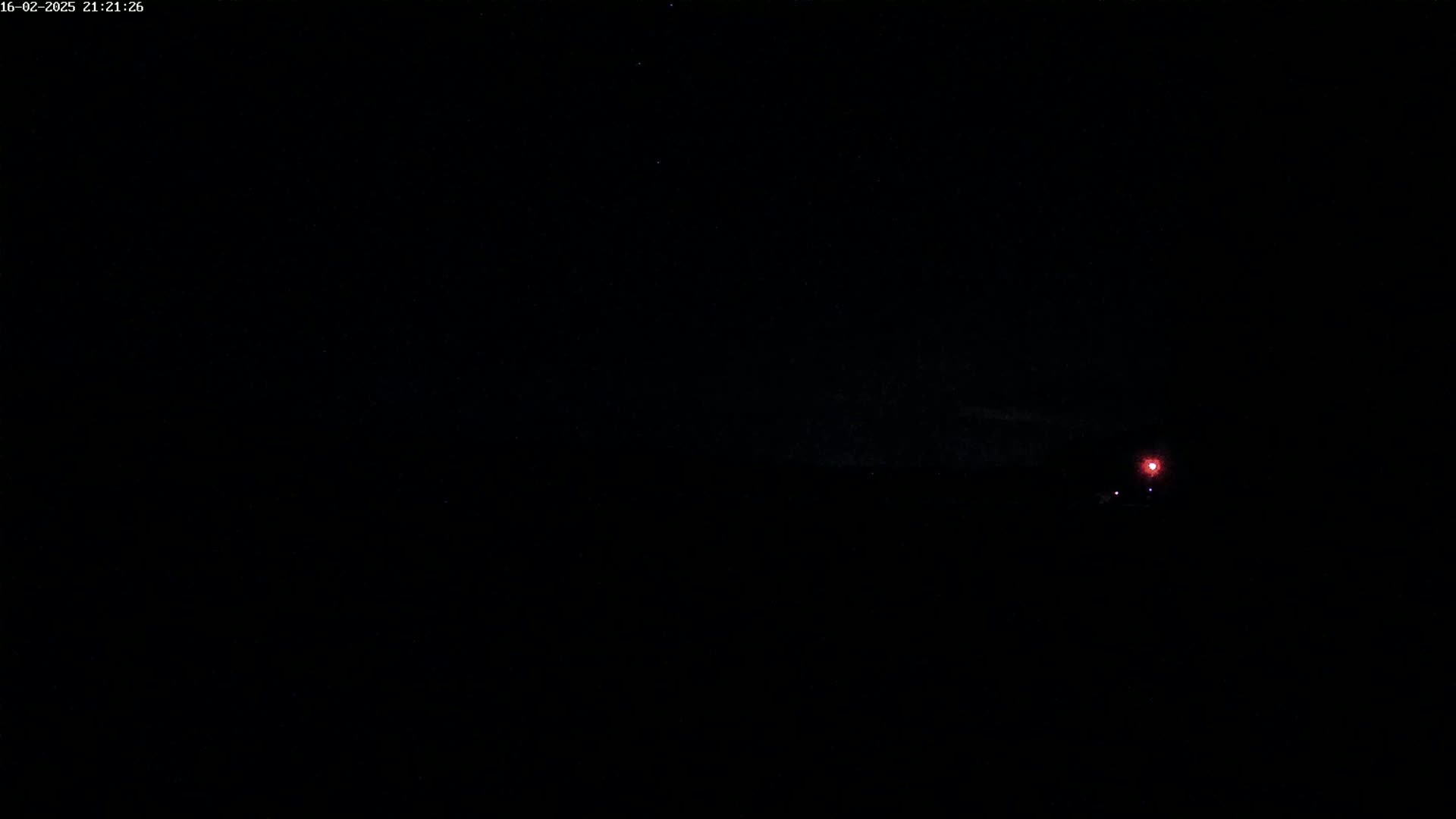 A dark, nighttime scene shows a single faint red light in the distance under a mostly clear sky.