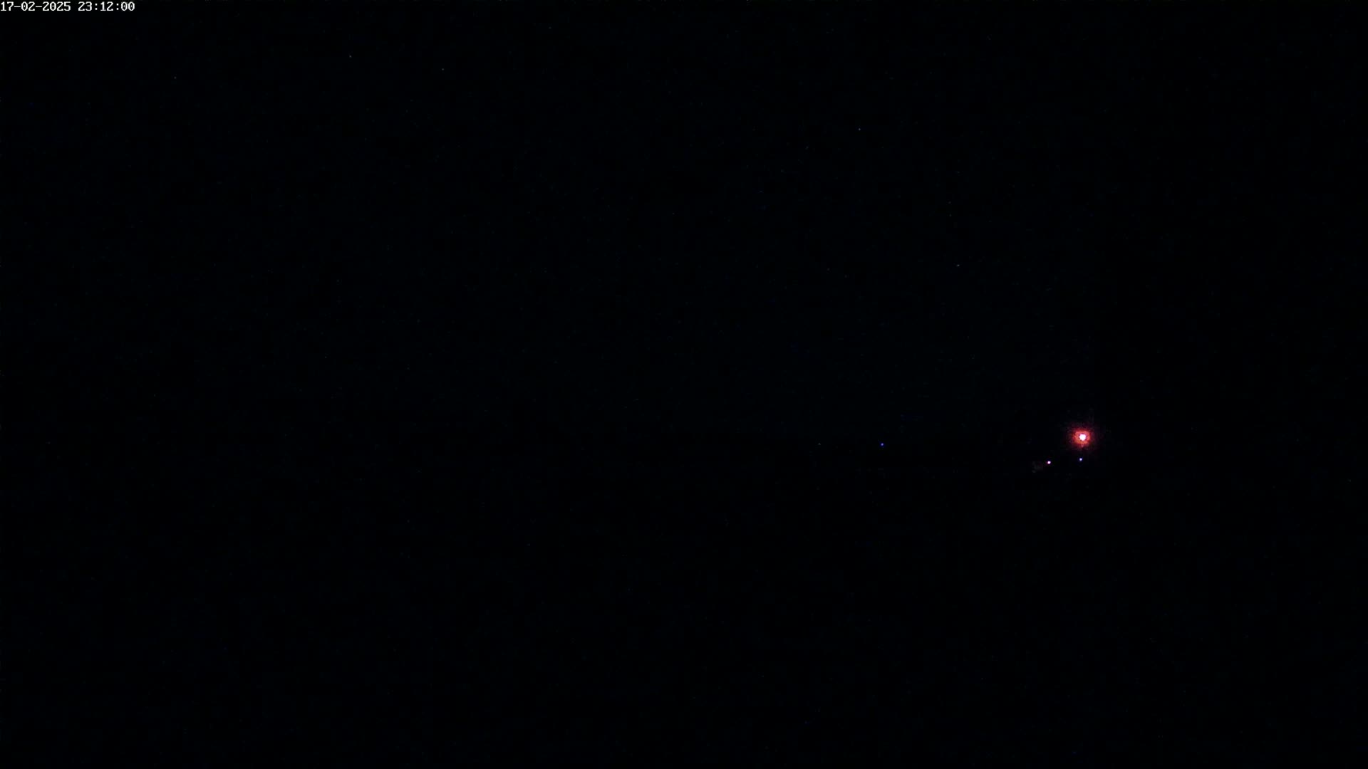 A dark nighttime scene shows a small, faint red light in the distance under a clear, starry sky.