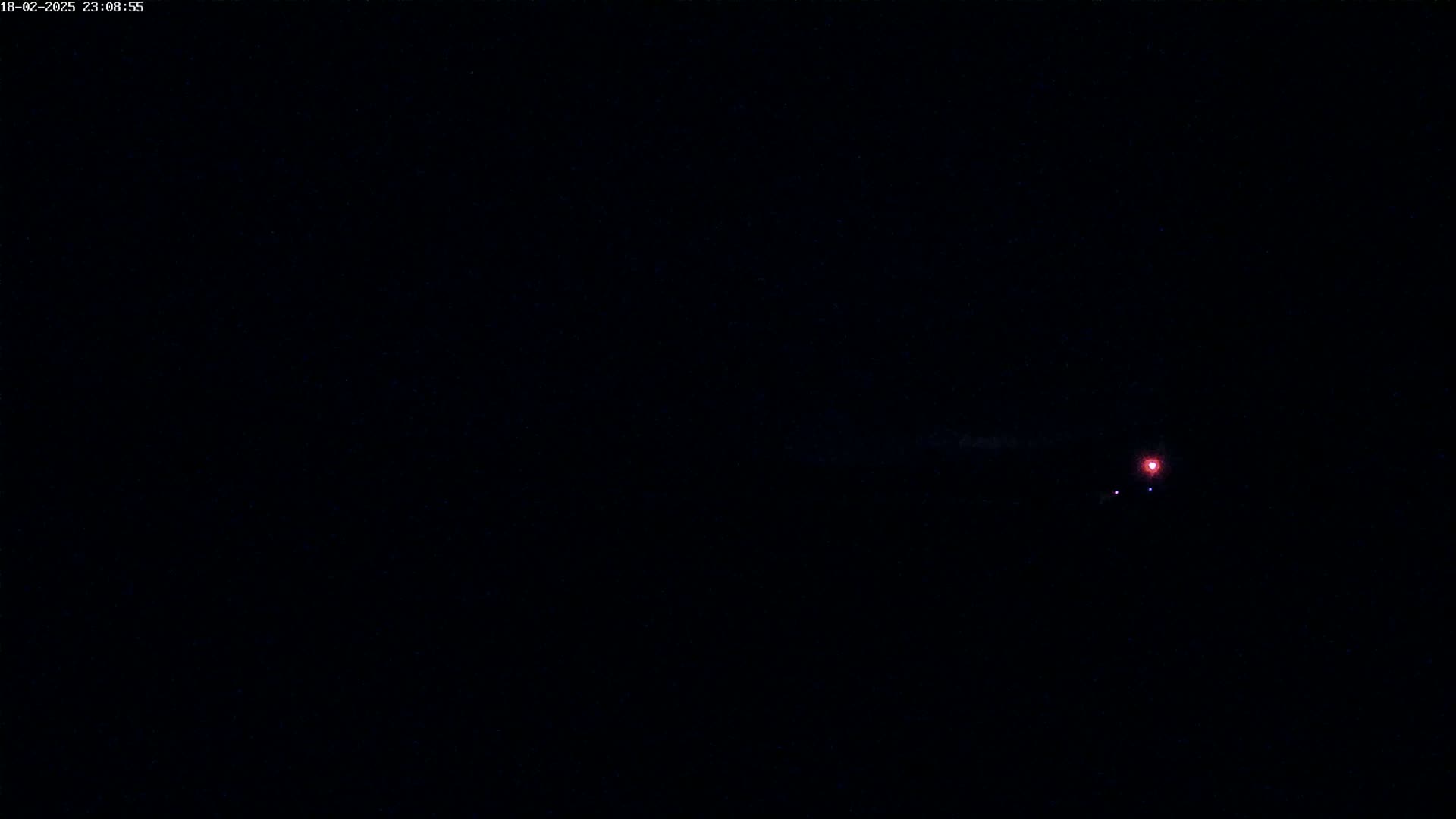 A small, reddish light is visible in the inky blackness of the night sky.