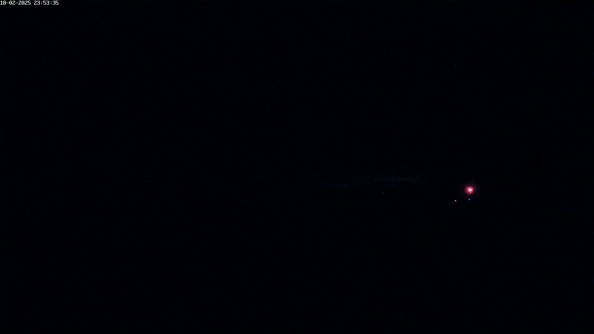A dark night sky shows a faint reddish light in the distance with some fainter lights near it.