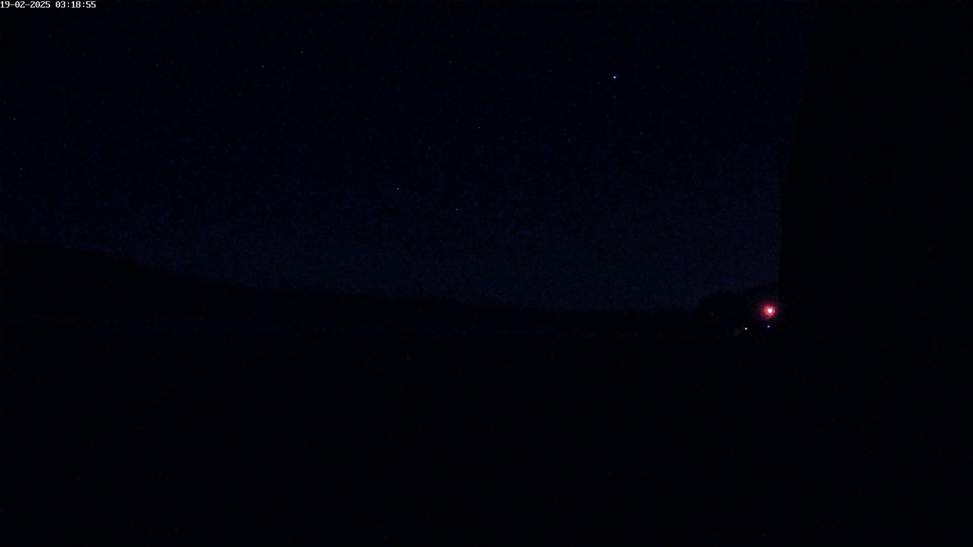 A dark, nighttime landscape is visible under a starry sky, with a single red light in the distance.