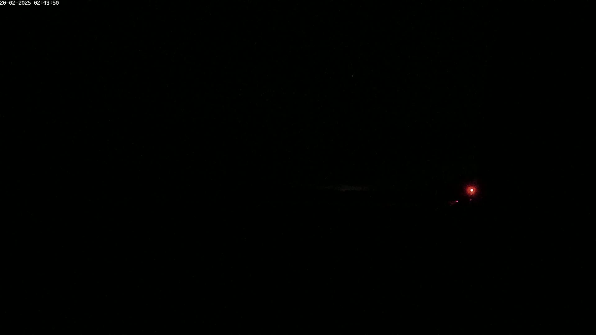 A faint red light is visible in the distance on a very dark, clear night.