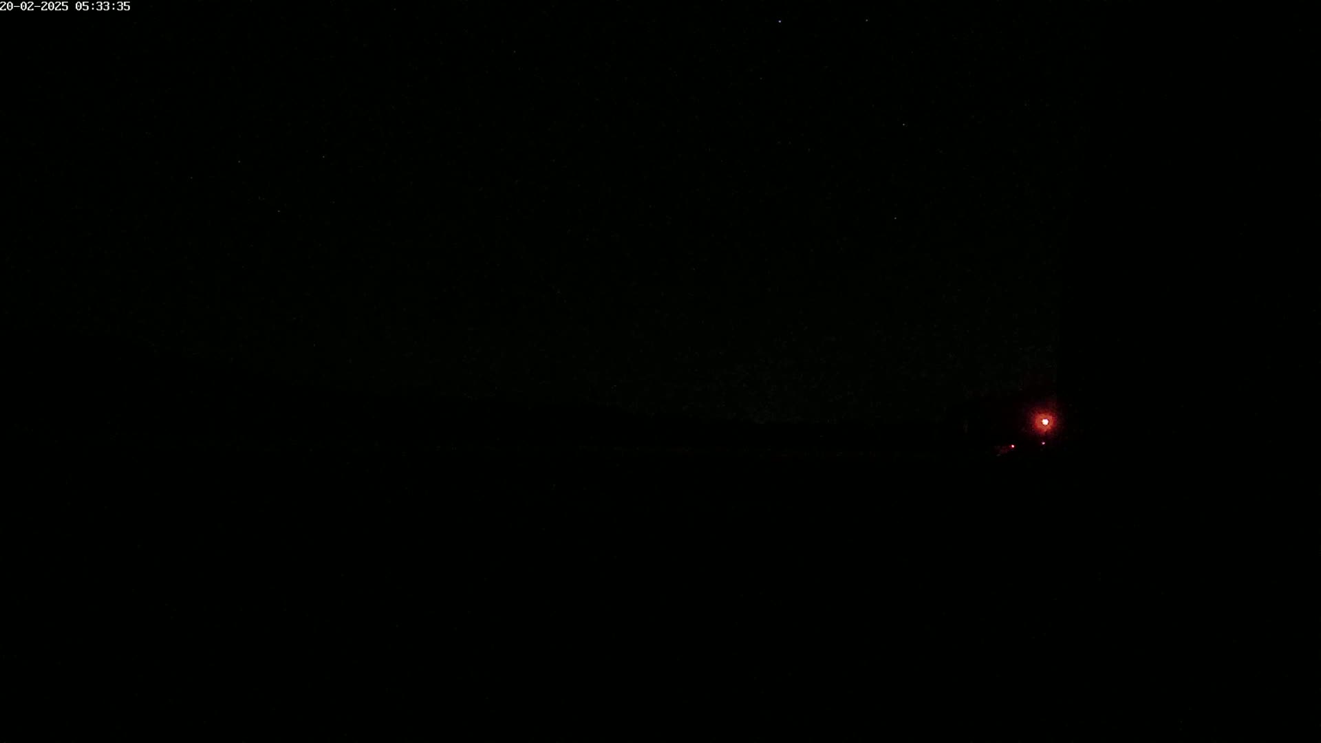A dimly lit nighttime scene shows a small red light in the distance under a dark, star-filled sky.