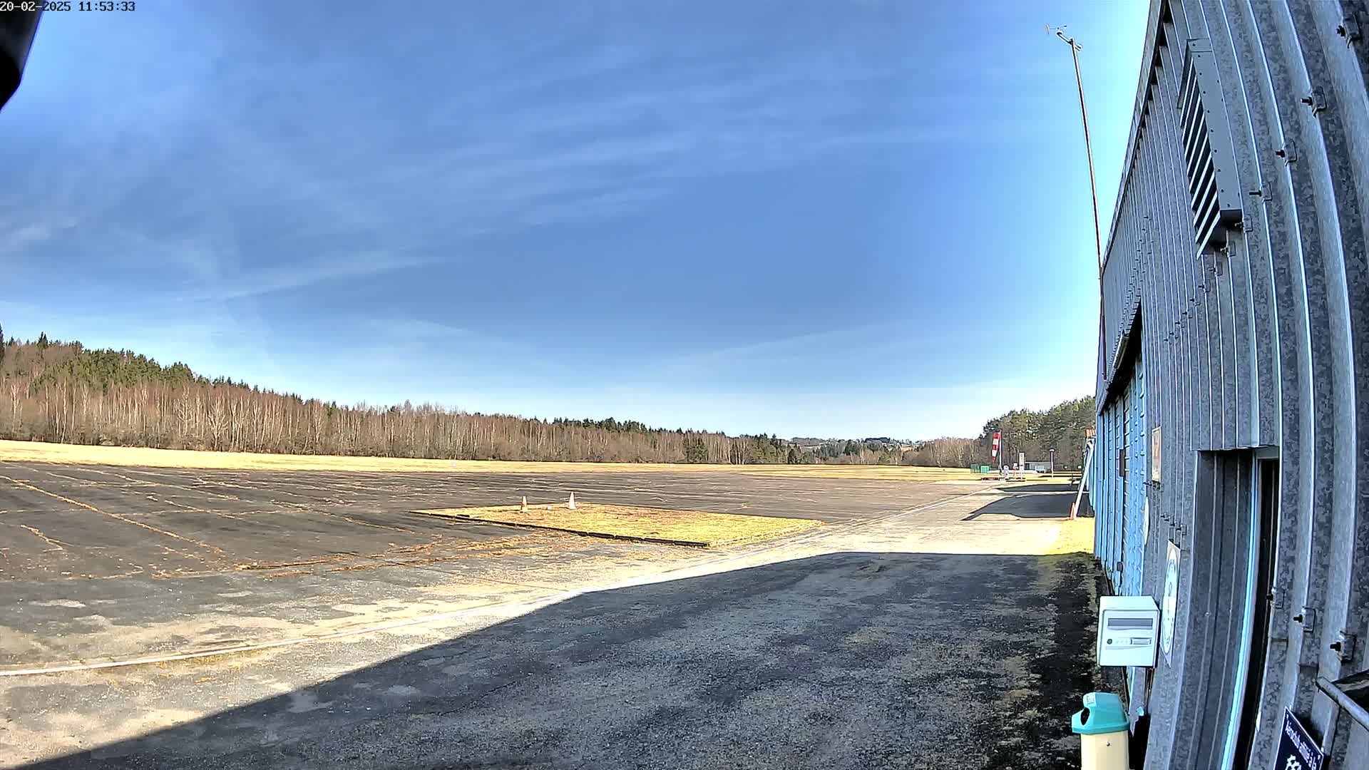 A large, empty tarmac area bordered by a line of trees under a mostly clear blue sky.