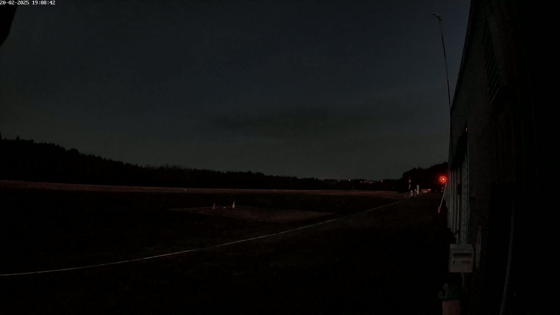 A dark, nighttime scene shows a flat, empty asphalt area next to a tall, dark building under a mostly clear sky.