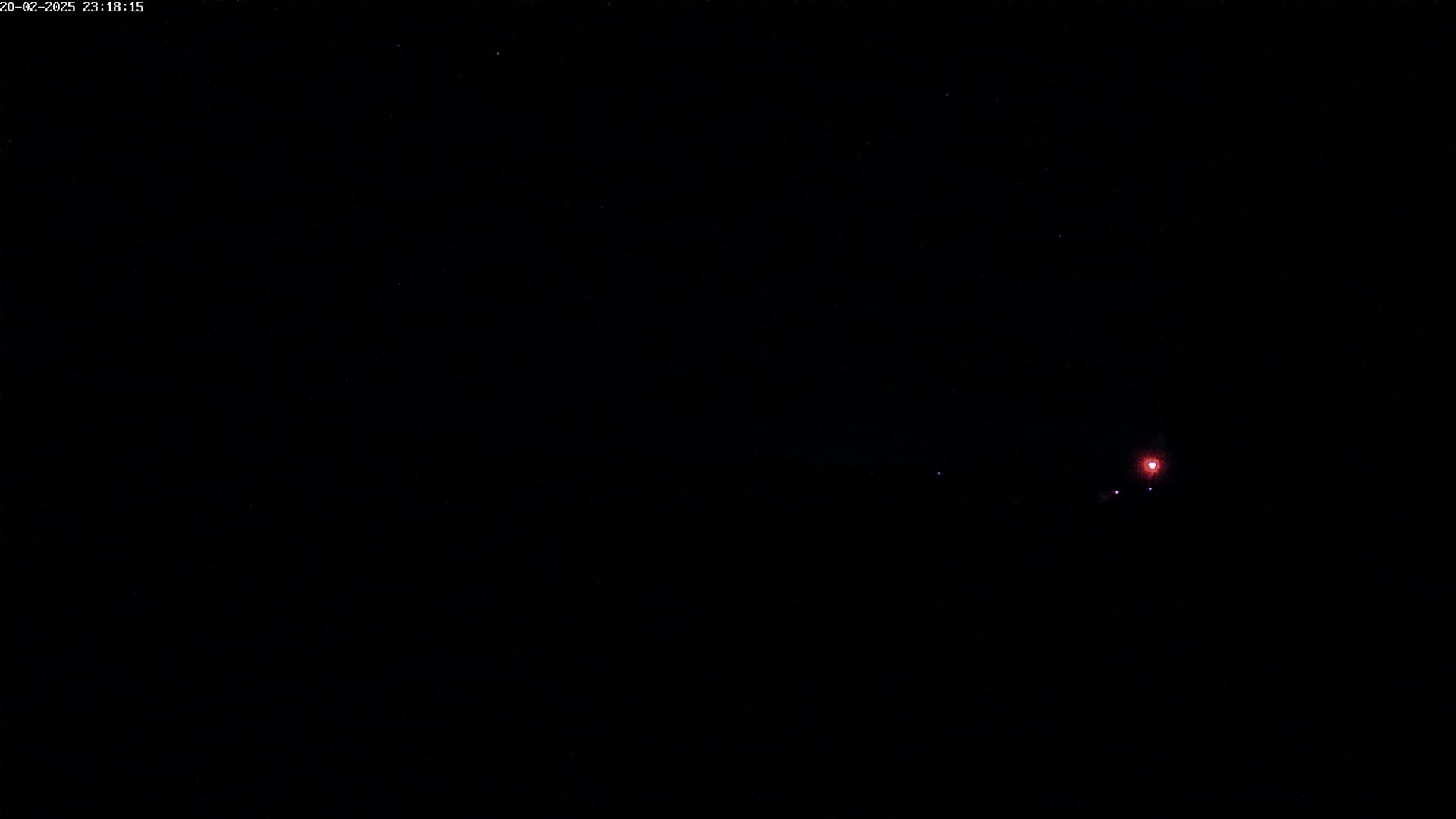 A small, reddish light is visible in the center of a dark, nighttime sky.