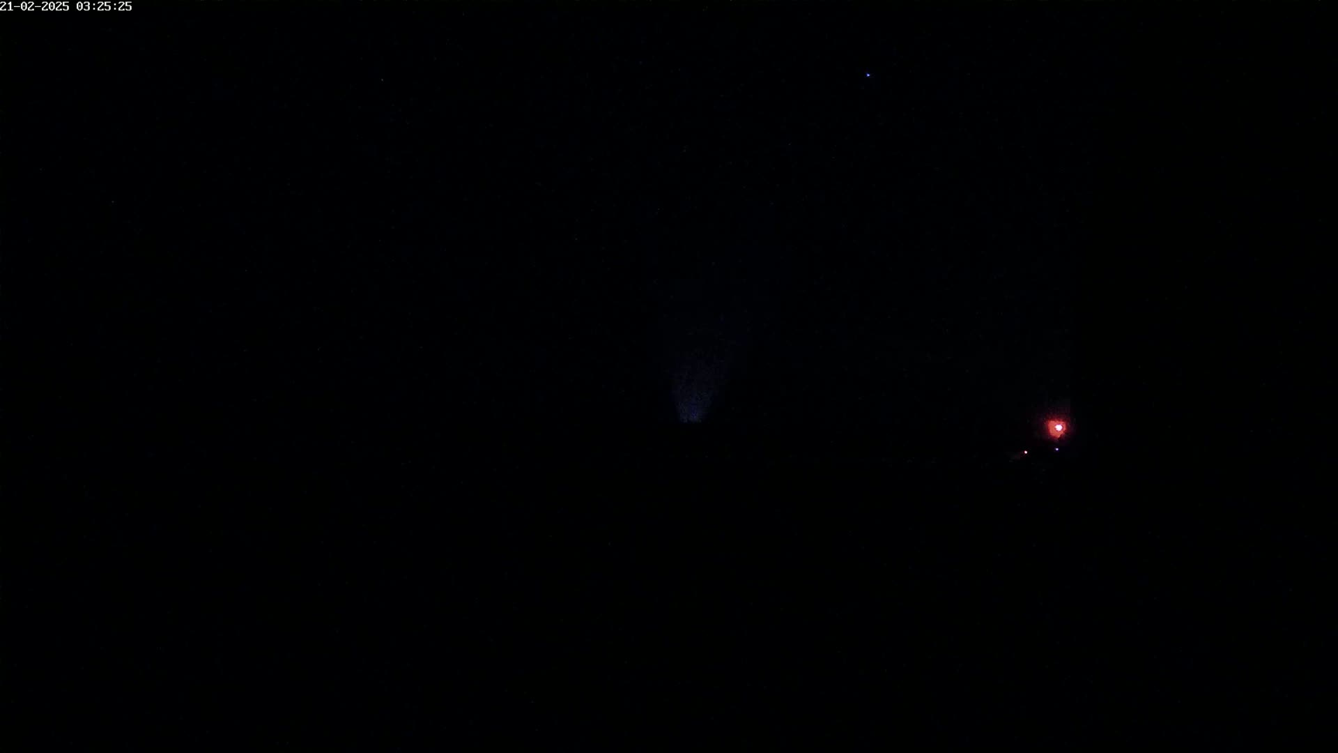 A dark night sky shows a faint, purplish light source and a small, reddish light source in the distance.