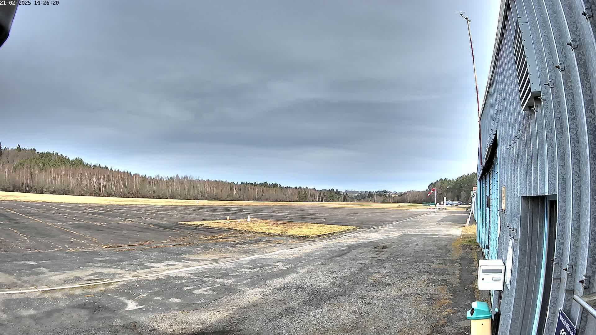 A tarmac airstrip with a grassy area and a metal hangar is visible under an overcast sky.