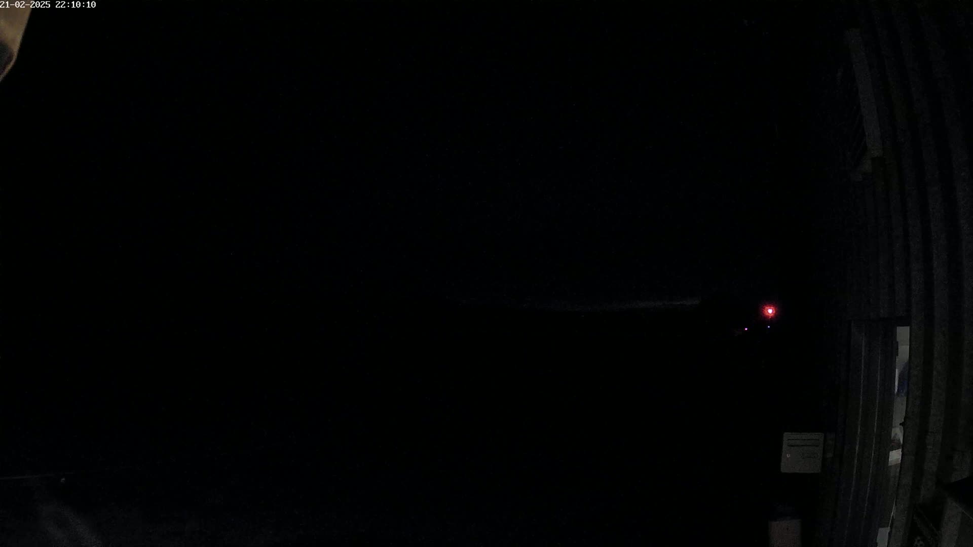 A dark, nighttime scene shows a faint red light in the distance and a portion of a corrugated metal building to the right.
