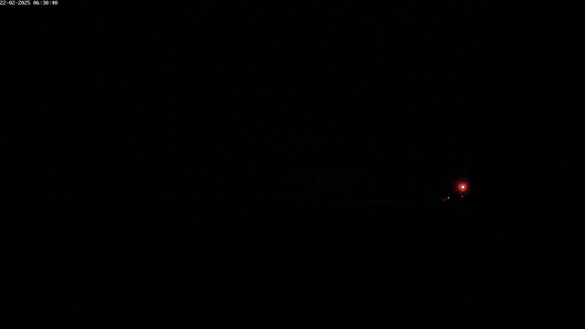 A single, faint red light is visible in the distance against a completely dark, nighttime sky.
