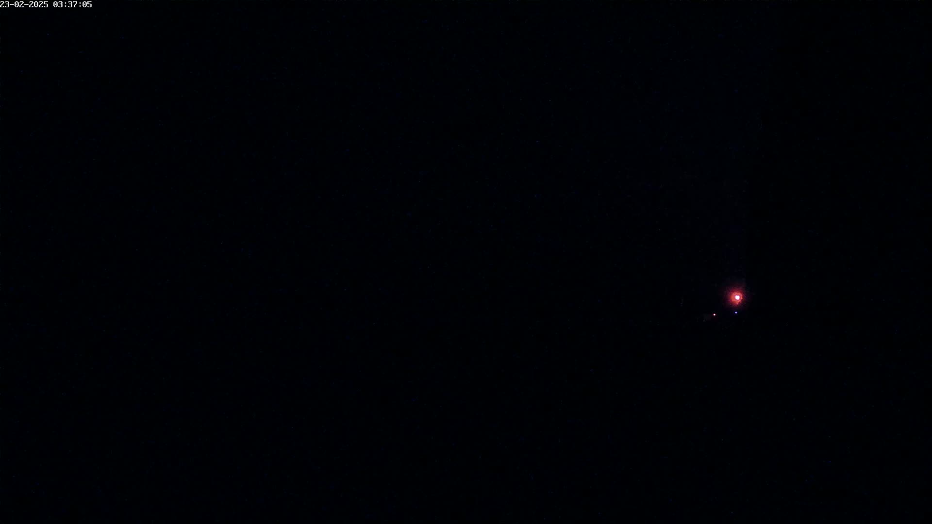 A small, faint red light is visible in the center of a completely dark, nighttime scene.