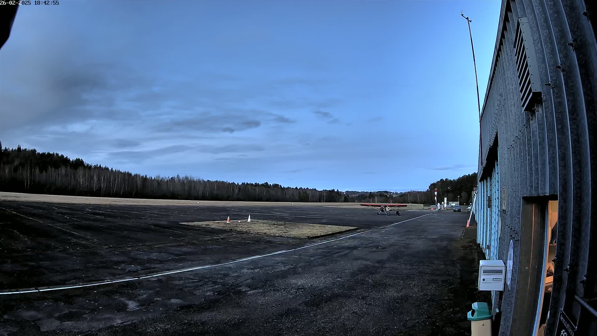 A small airplane sits on a tarmac next to a hangar under a mostly clear, twilight sky.
