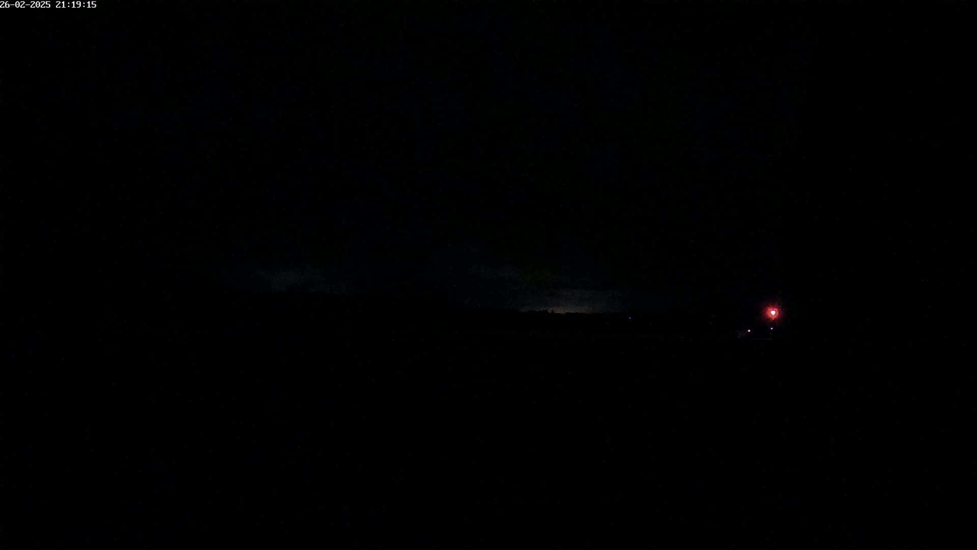 A dark, nighttime landscape is shown with a faint, distant light source and a possible storm in the distance.