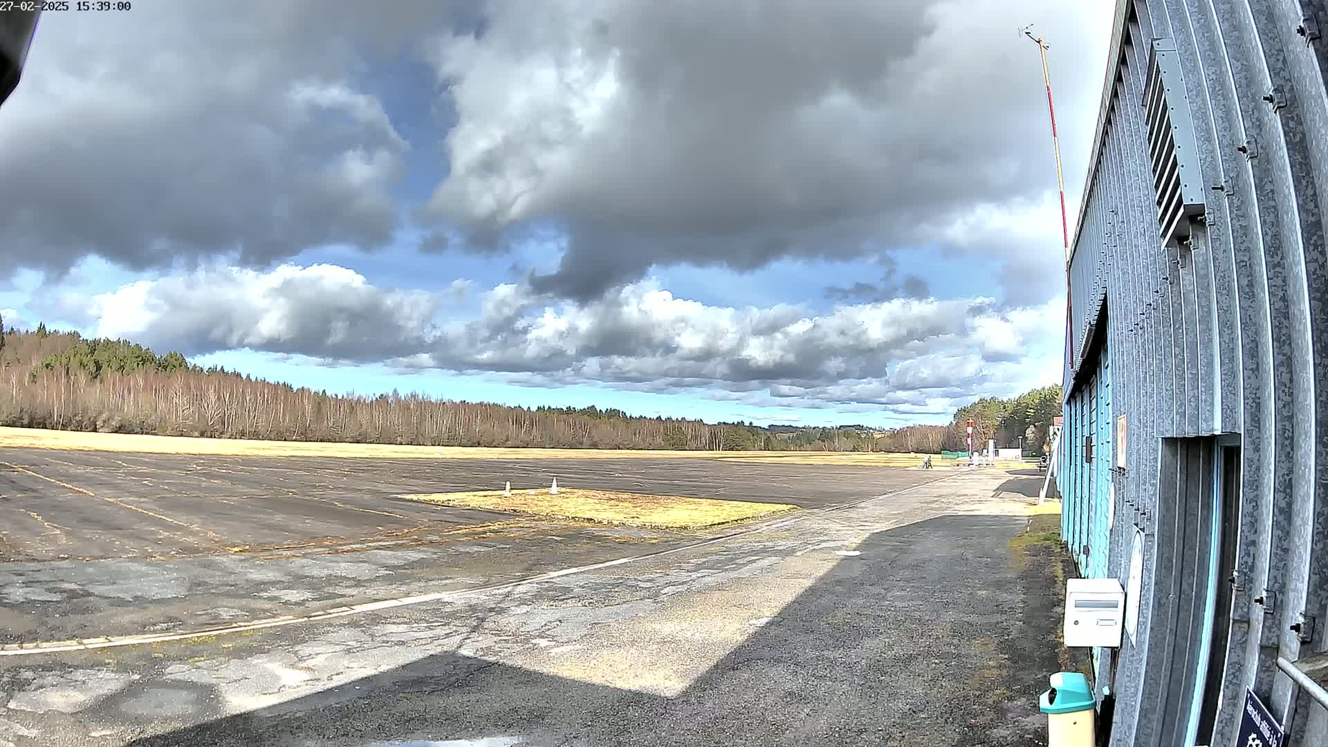 A mostly sunny day with partly cloudy skies over a small airfield with a hangar in the foreground.