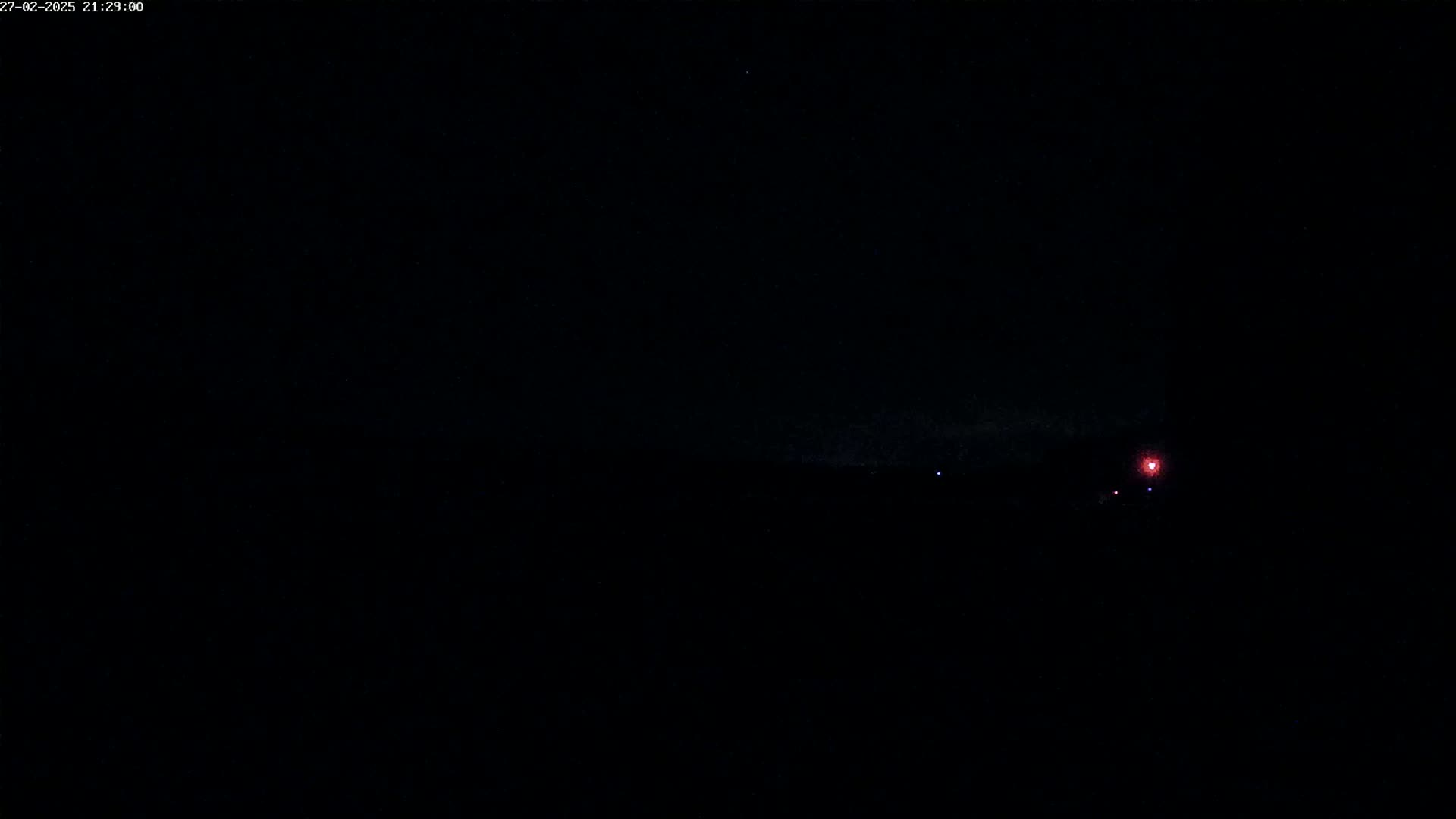 A dark, nighttime scene shows a faint red light in the distance, possibly a light source on the horizon.