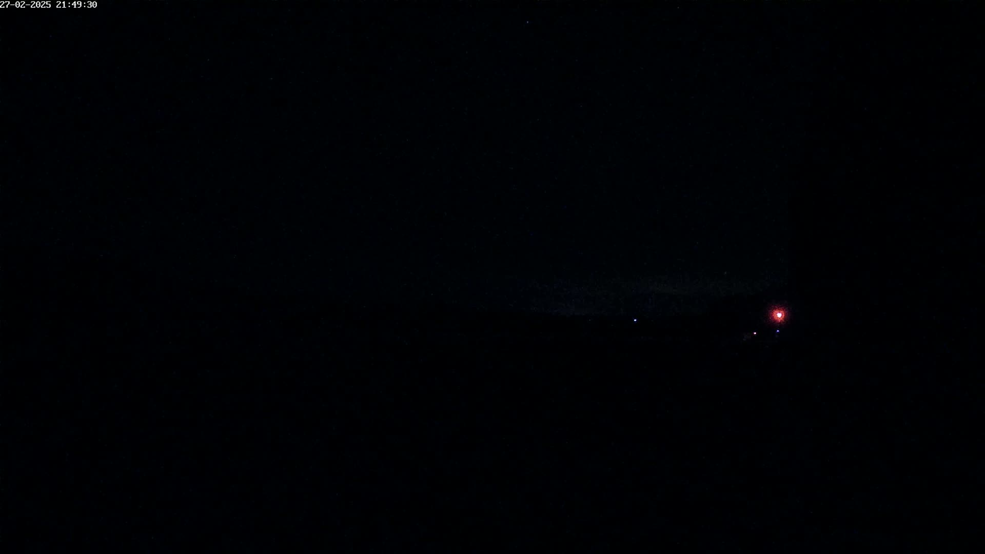 A dark, nighttime scene shows a faint red light in the distance under a mostly clear sky.