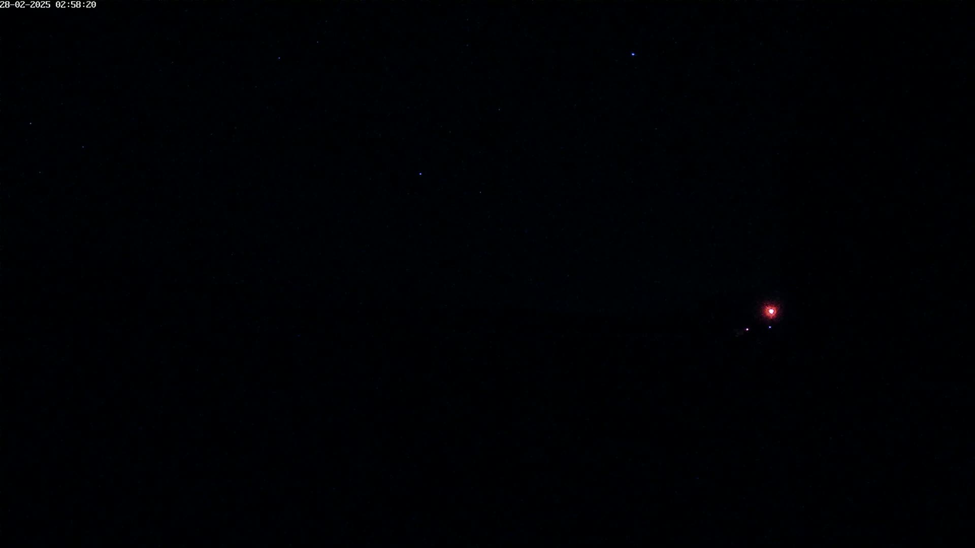 A dark night sky with a few visible stars and a faint reddish light in the lower right.